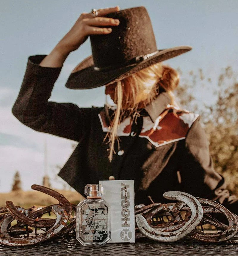 Woman wearing a cowboy hat with a bottle of HOEY west desperado perfume bottle and horseshoes in the foreground.