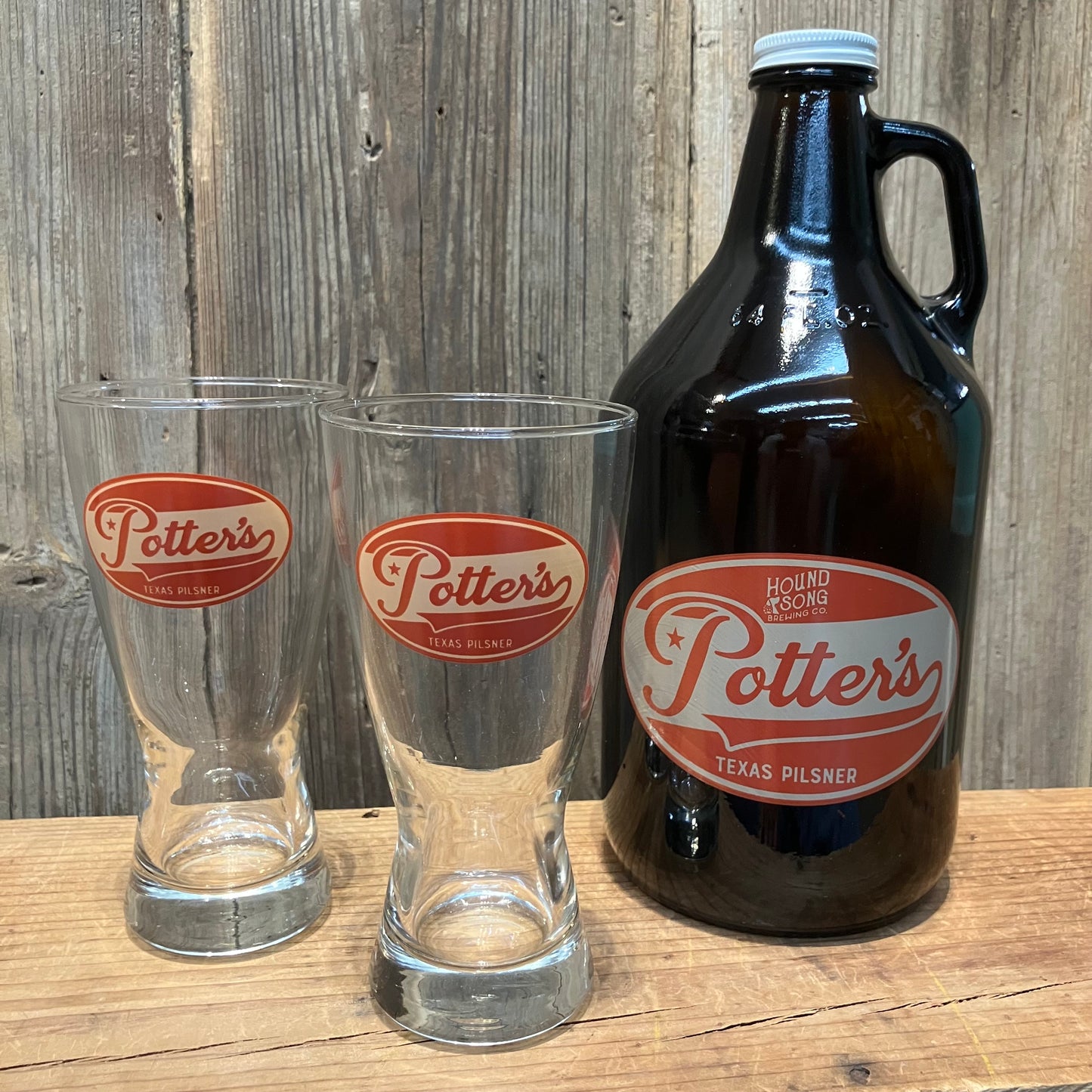 Two Potter's Texas Pilsner glasses and a growler gift set on a wooden surface with a wooden background.