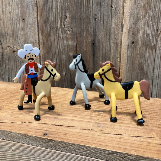 group of bendable toy horses with one cowboy figure on wooden background. Bendable Horses. Cowboys and cowgirls sold separately.