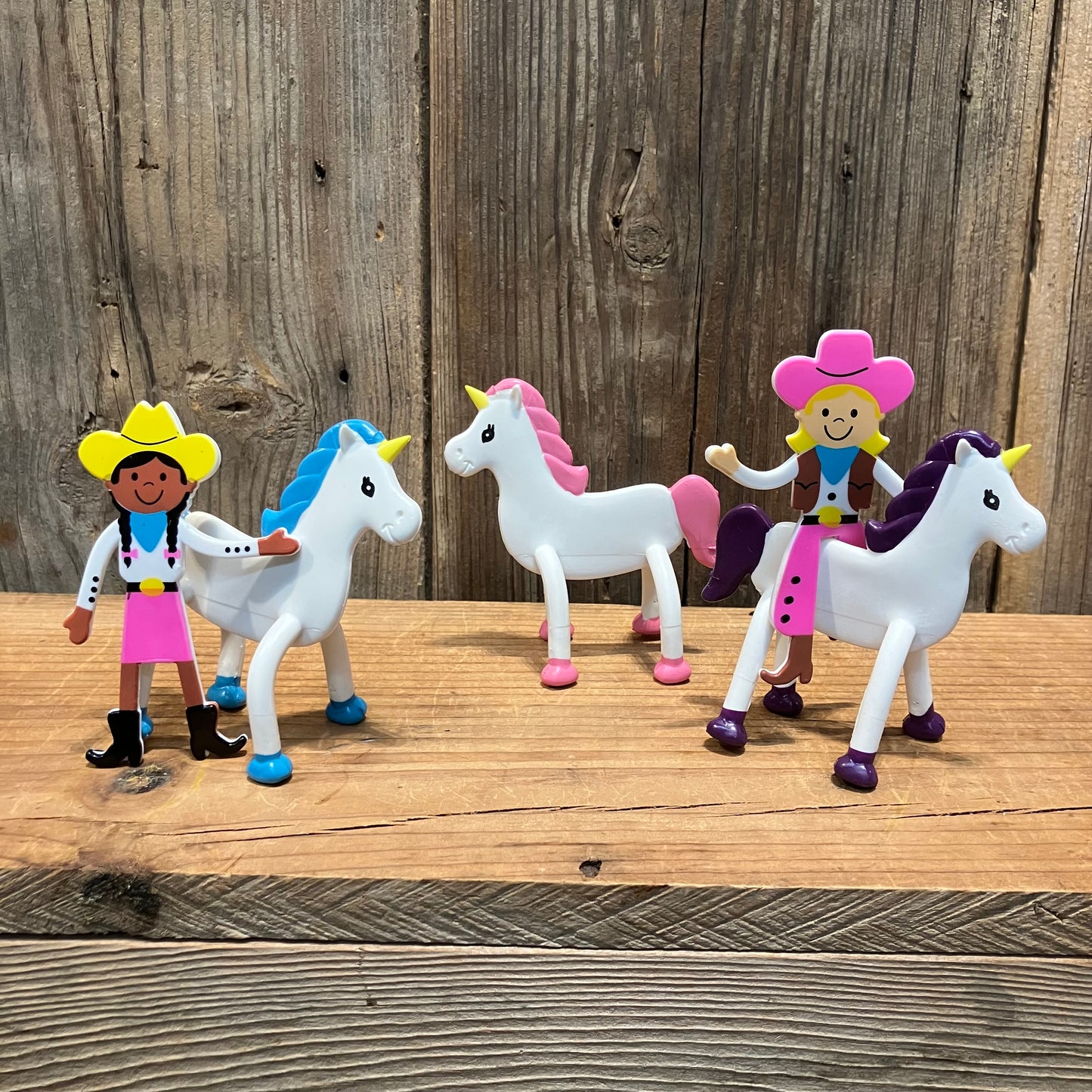Bendable cowgirl toys standing beside white unicorn horses with colorful manes