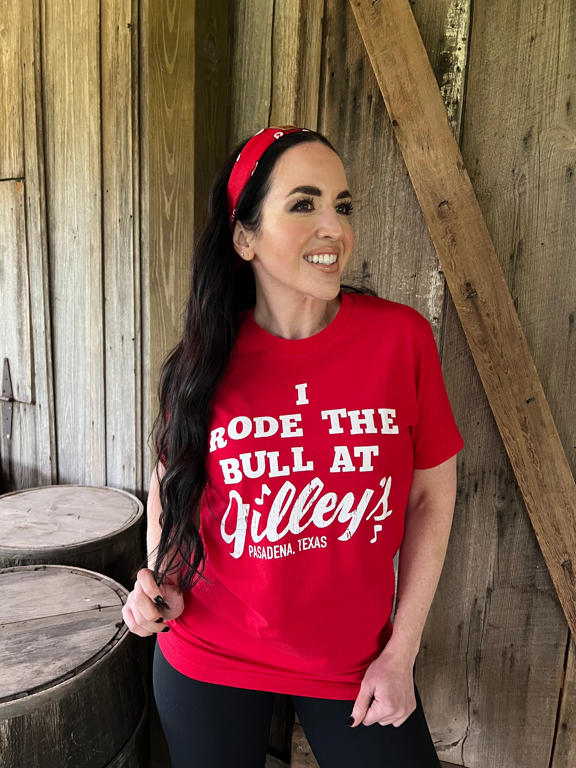 Woman wearing red Gilley's "I Rode the Bull" shirt standing in front of wood wall