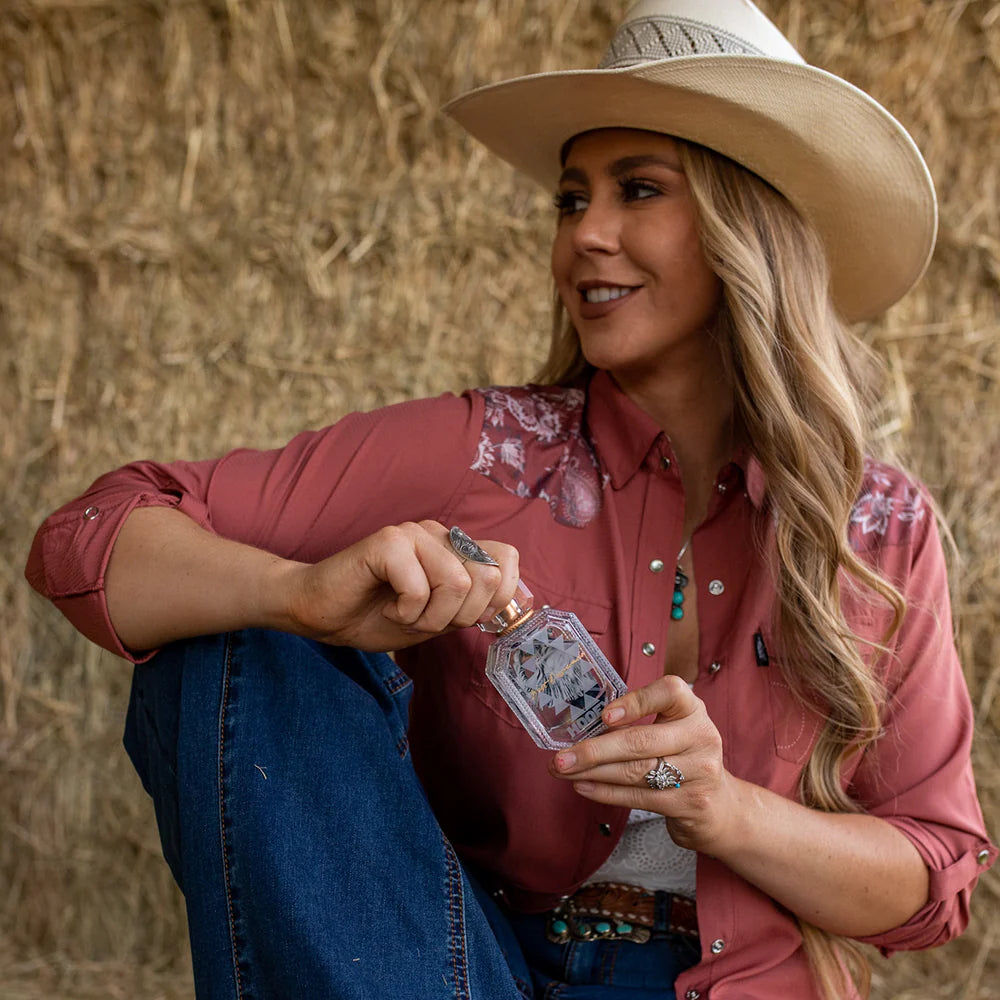 Woman in cowboy hat and pink shirt holding a card in front of a hay bale.